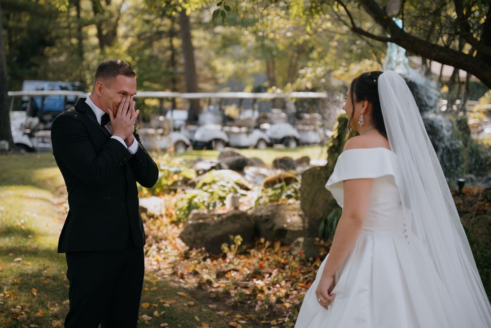 A wedding couple walks through a sunlit autumn park surrounded by fallen leaves and trees.