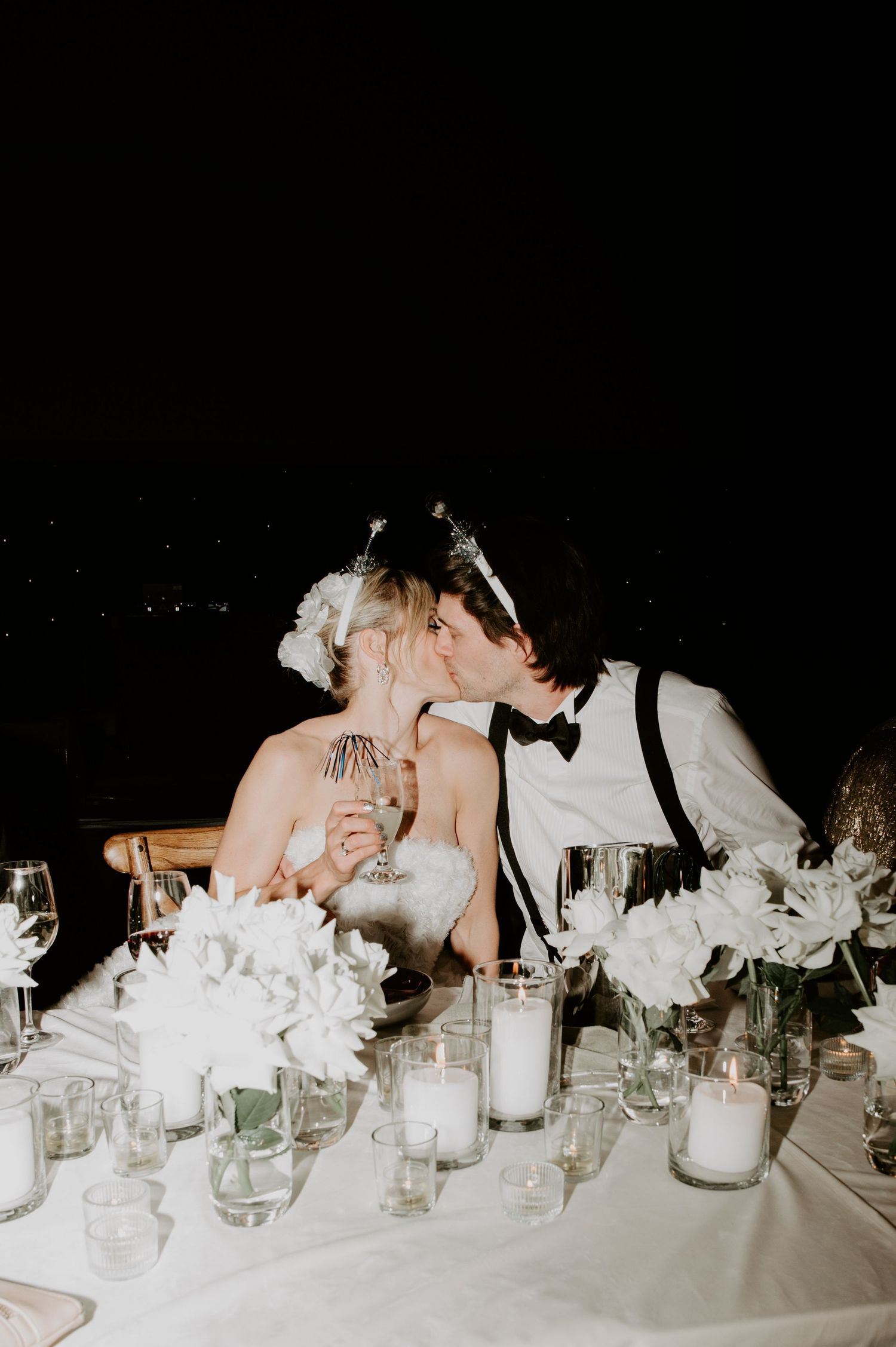 A romantic table setting at a wedding reception with white floral centerpieces and glowing candles in glass holders.