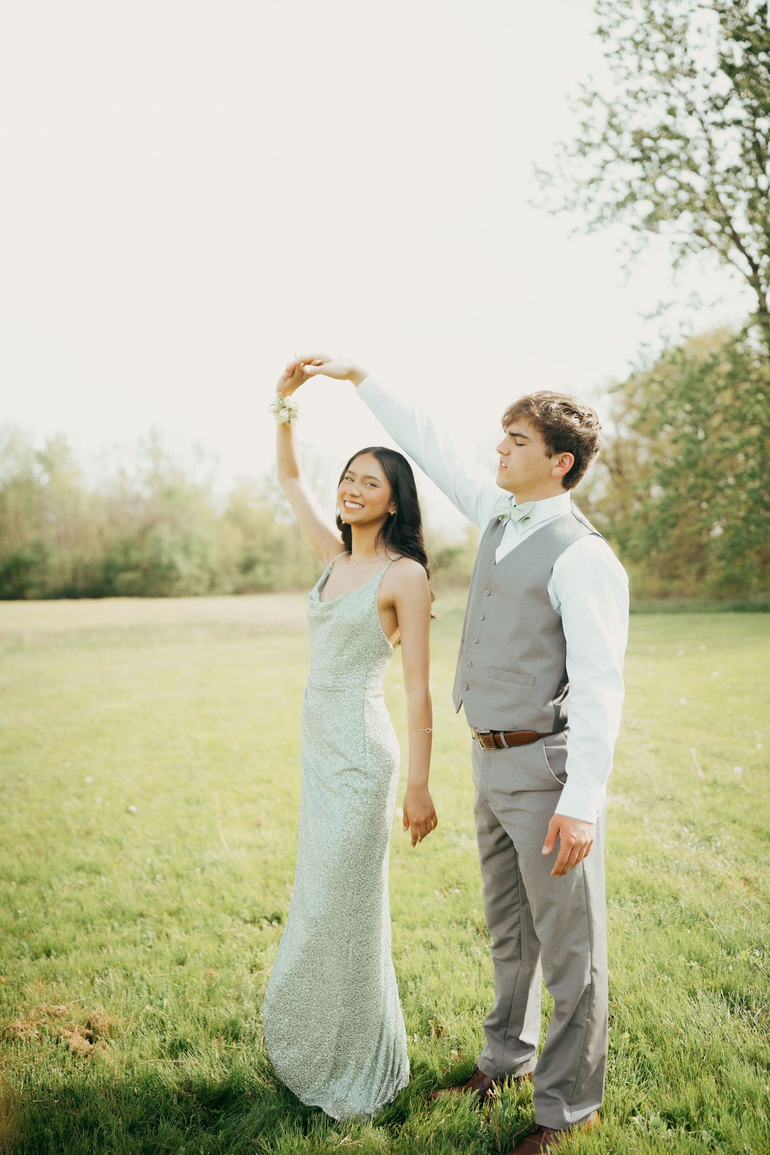 A couple in wedding attire dances joyfully together in a sunlit grassy meadow on their special day.