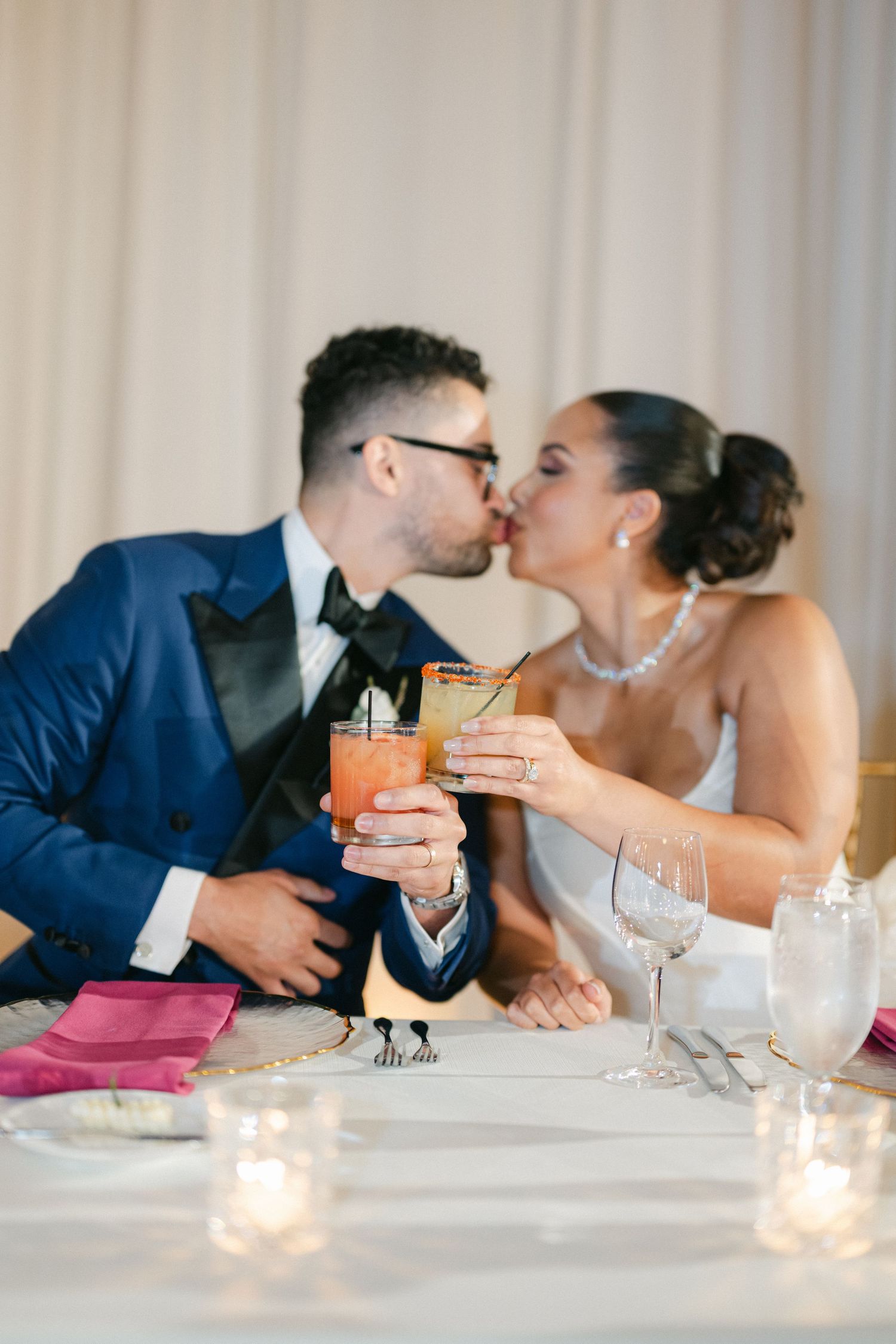 Romantic couple shares intimate kisses across a candlelit dinner table with cocktails.