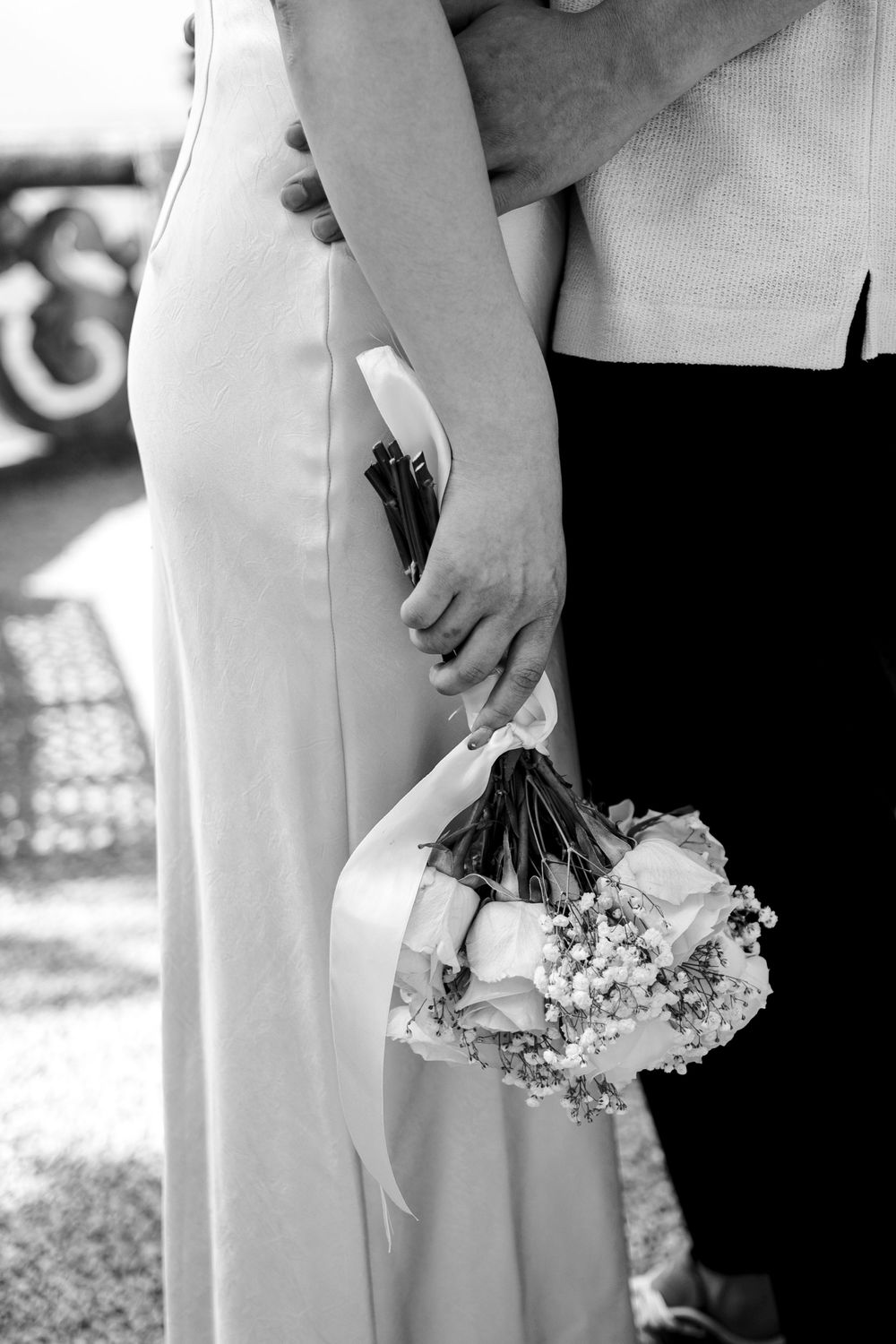 Black and white image showing hands holding a delicate bouquet of white flowers against formal attire.