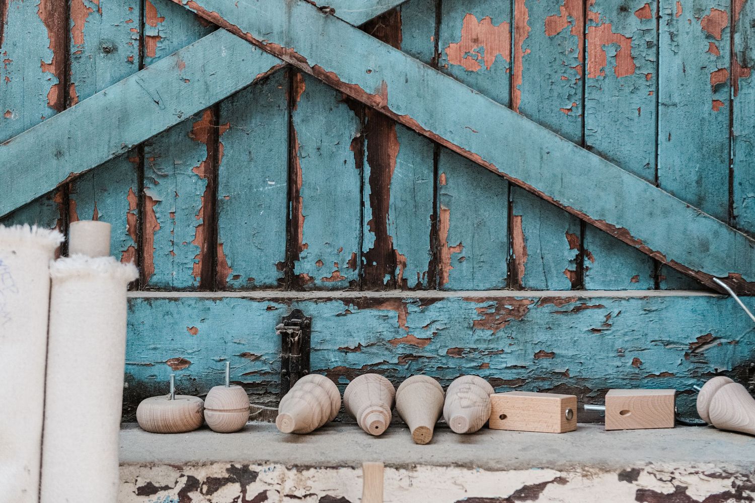 Row of freshly milled sofa legs lined up against a weathered blue wooden door with peeling paint.