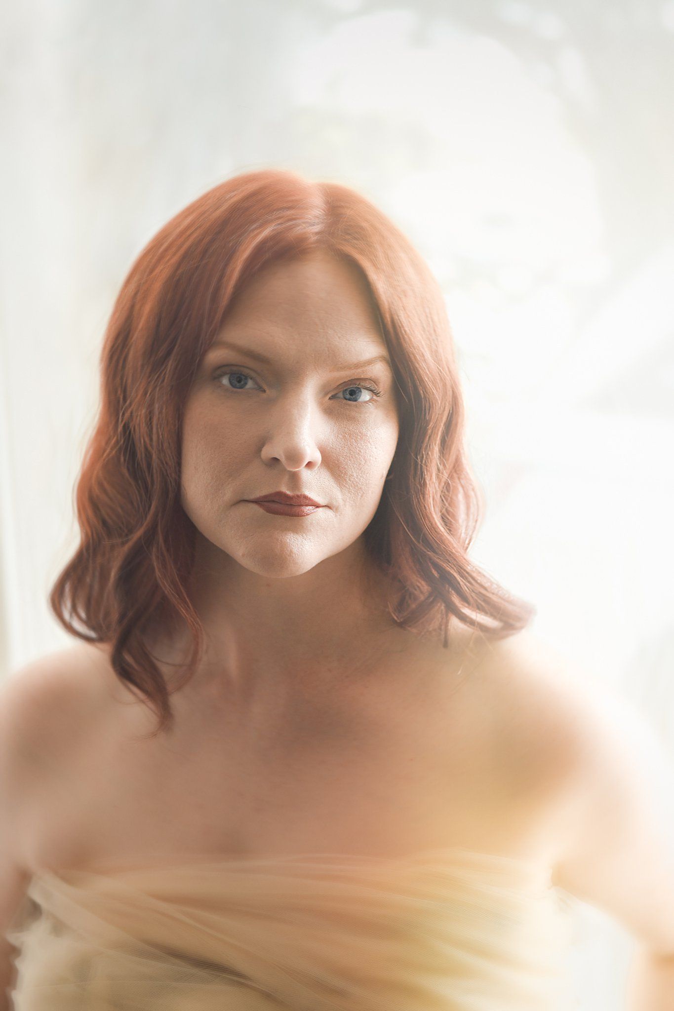 Ethereal portrait with soft lighting captures model in delicate white wrap against light backdrop.
