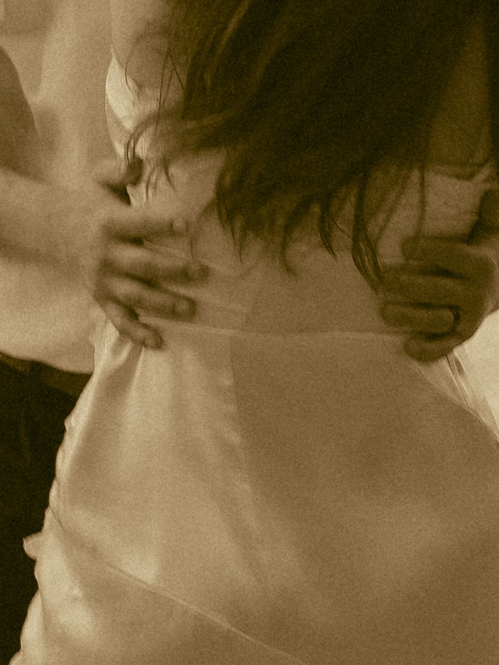 Sepia-toned close-up of a couple slow dancing, hands gently holding a woman's waist in a white dress.