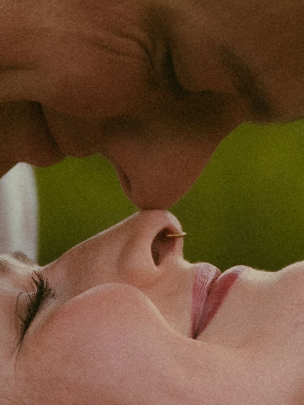 Two people sharing a tender kiss, with one person lying down and the other leaning in, set against a soft green background.