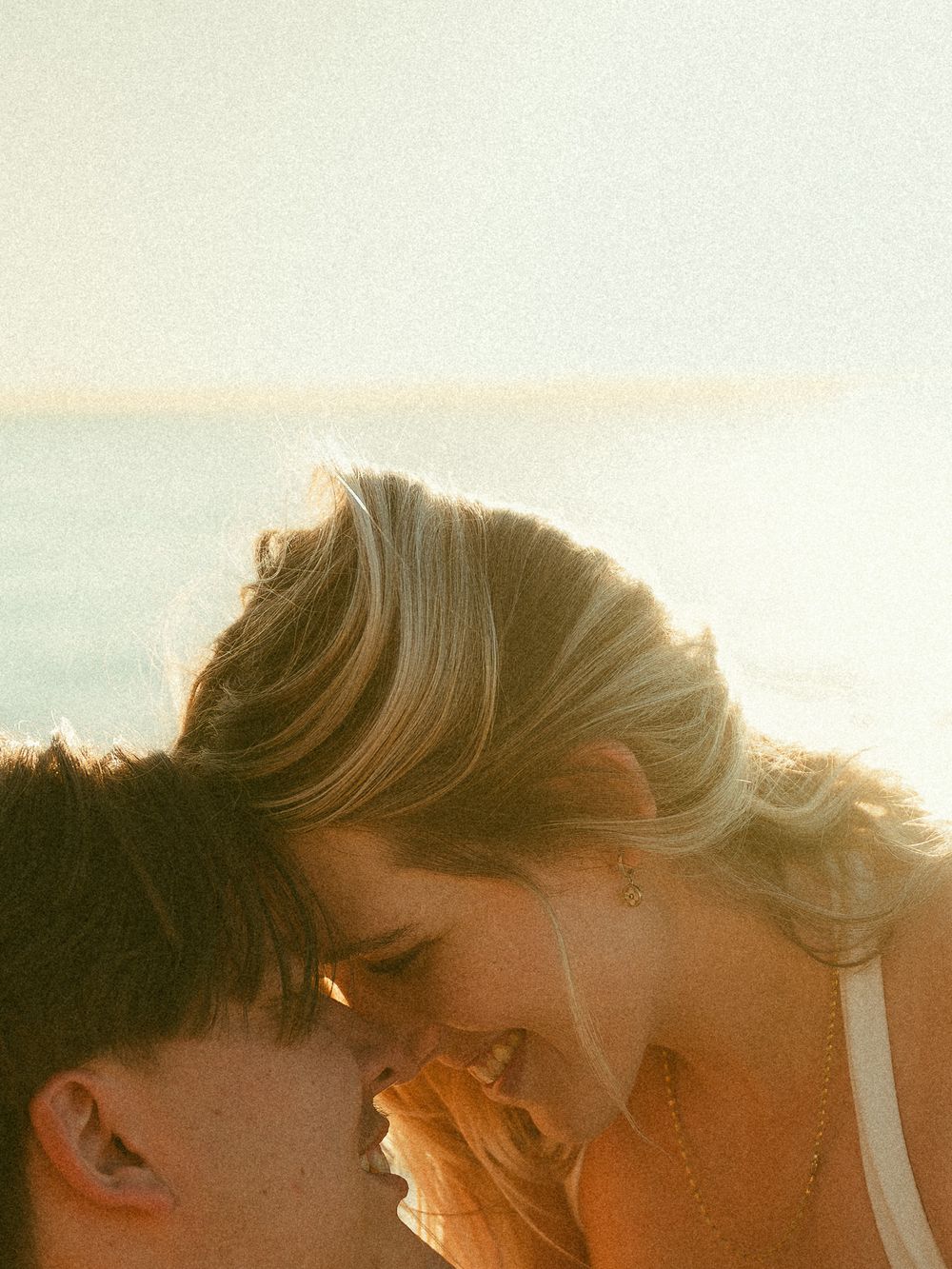 Romantic couple sharing a tender moment close together with glowing sunset light over the ocean.