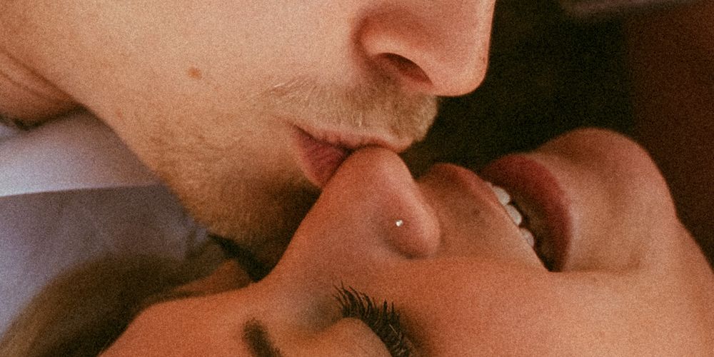 Close-up of a couple sharing an intimate kiss, with the woman smiling and wearing a nose ring.