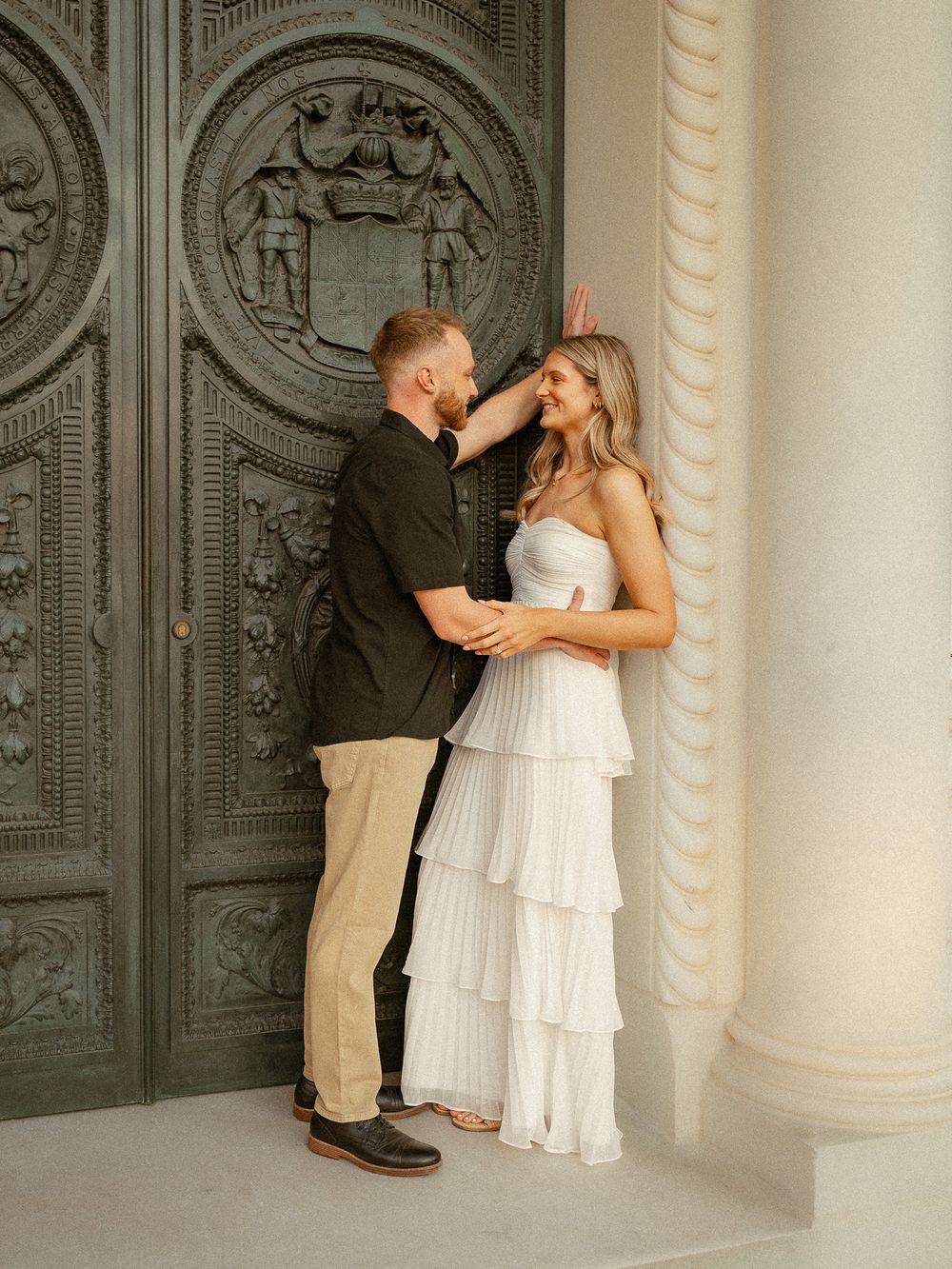 Couple posing romantically in front of ornate green doors and white columns in engagement photo.