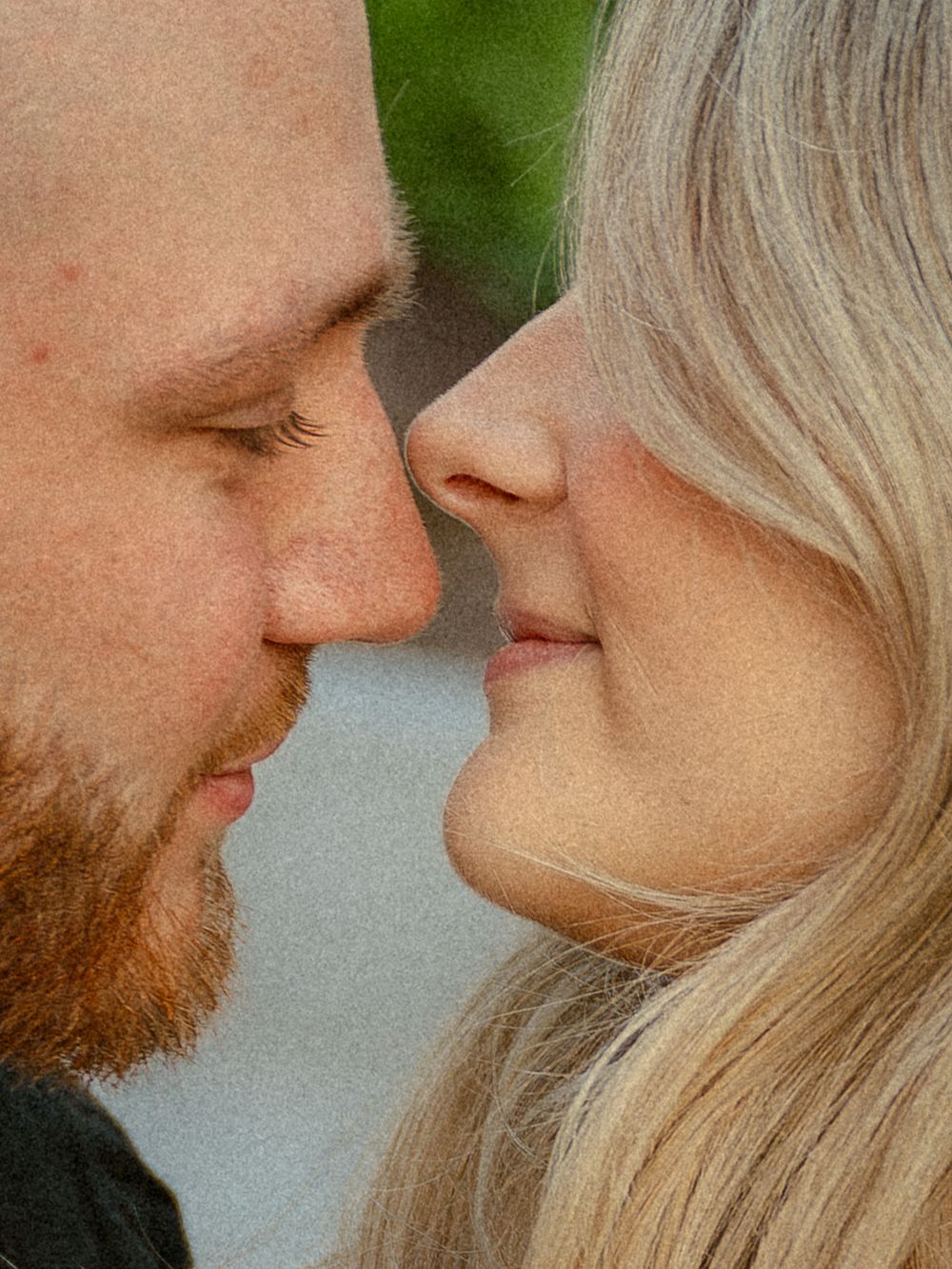 Close-up of a couple leaning in for a kiss, man with red beard and woman with blonde hair.