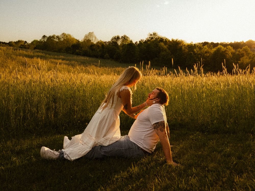 Romantic couple sharing tender moment sitting in sunlit meadow at golden hour.