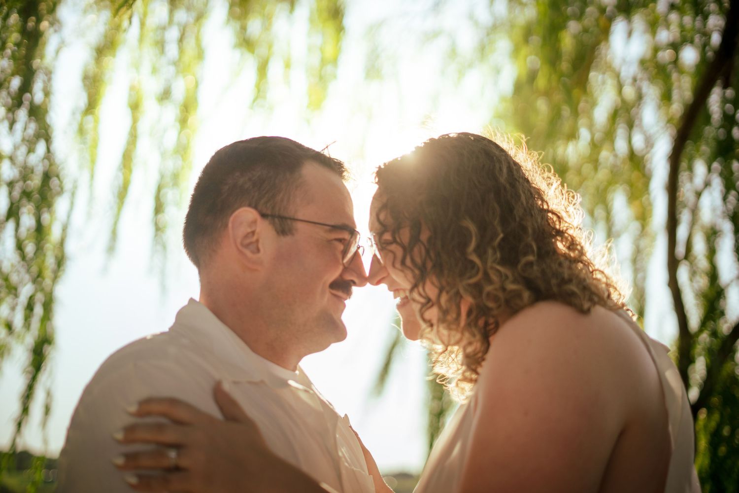 a woman leaning into a mans arms while they sit on the ground in a field. a very aesthetic couples photo, shot from behind.