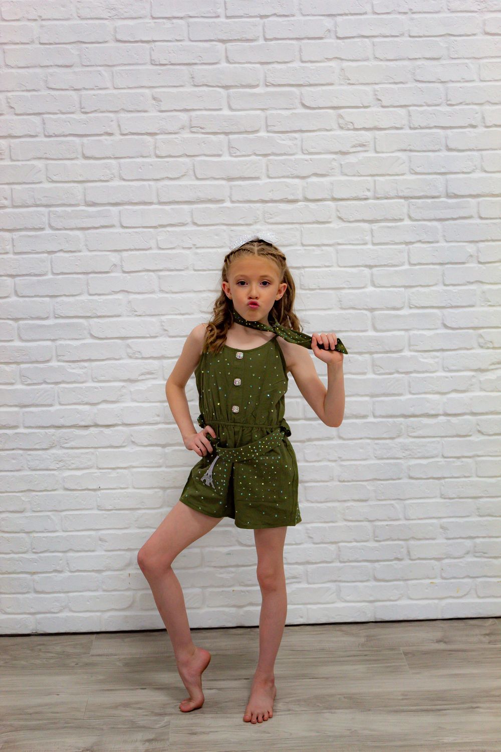 Young dancer in olive green outfit strikes dynamic poses against white brick wall.