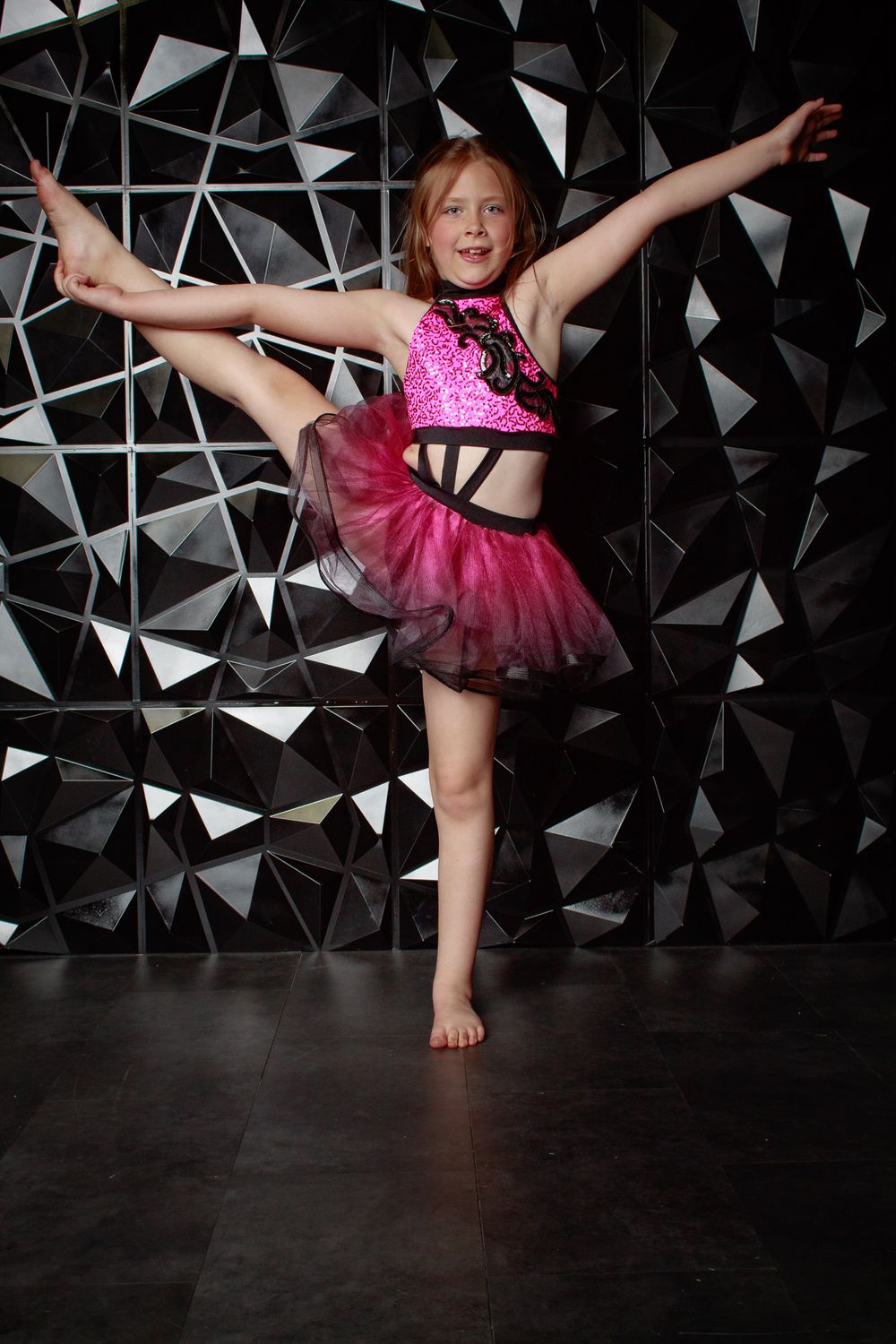 A dancer in a pink tutu performs dynamic movements against a dark background with triangular patterns.