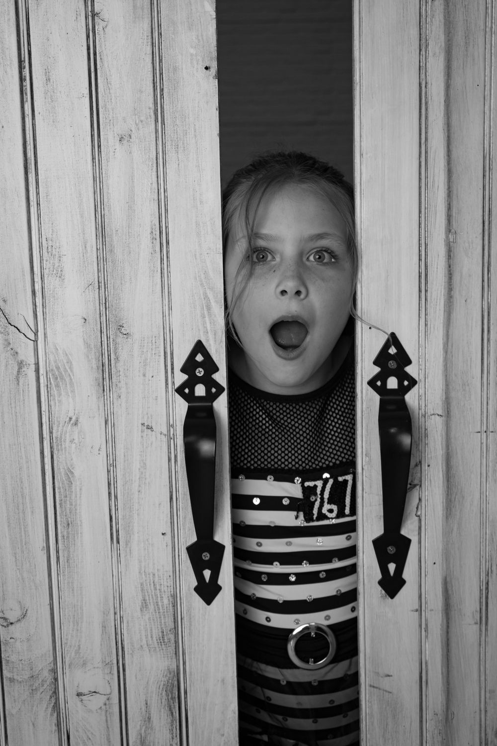 Playful peek-a-boo poses through white wooden slats with decorative eye cutouts.