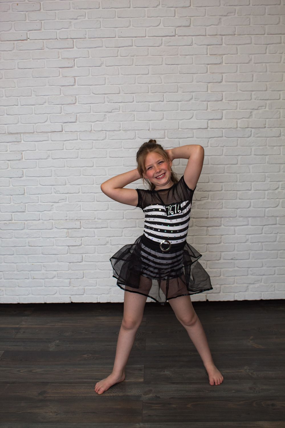 Energetic dance poses in a black and white striped costume against a white brick wall.