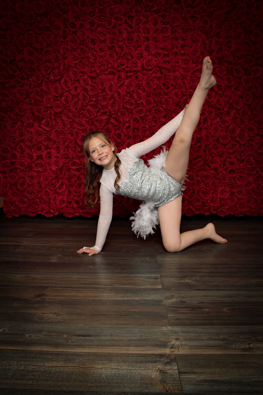 A dancer in a silver costume performs artistic floor movements on wooden flooring with red backdrop.