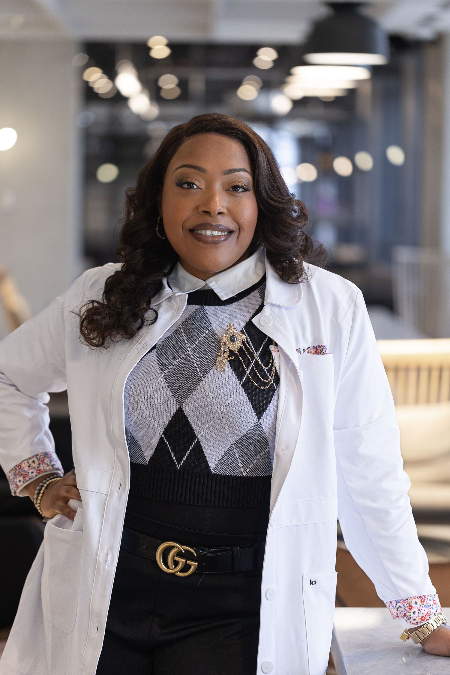Healthcare professional wearing a white lab coat, argyle sweater vest and Gucci belt in a modern office setting.