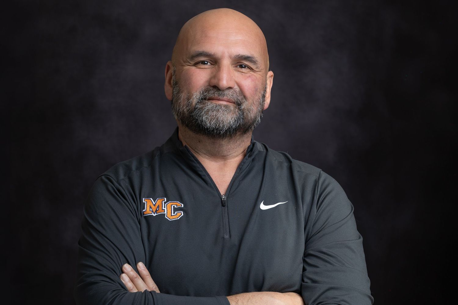 Professional headshot of a person in a black Nike shirt with crossed arms against a dark background.