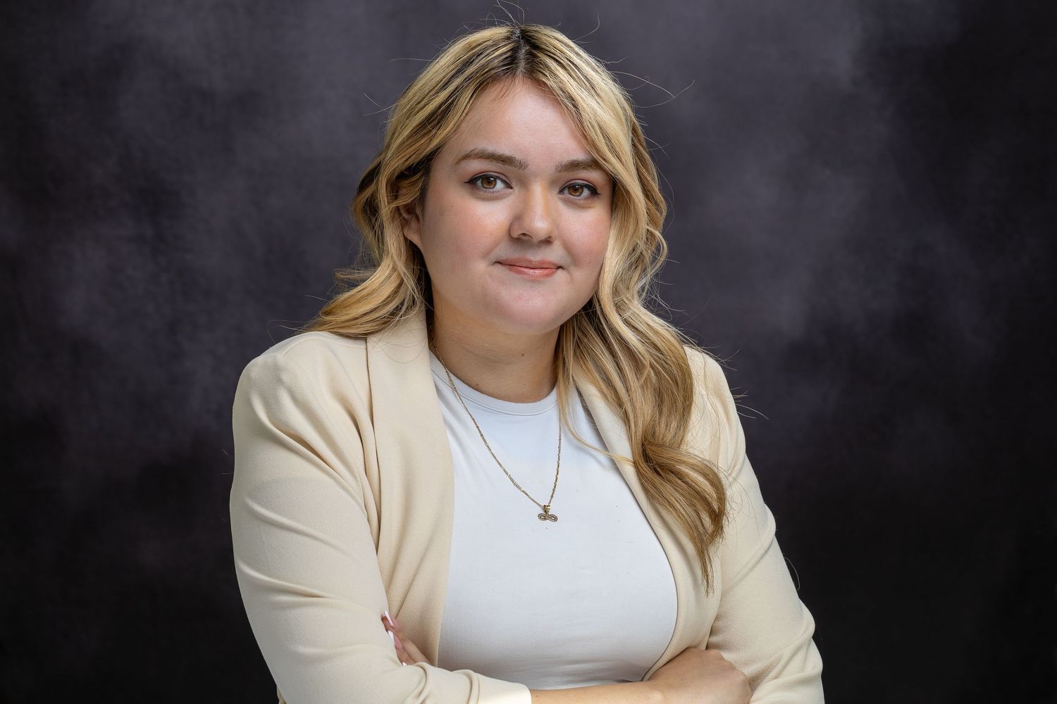 Professional headshot portrait of a person in a cream blazer and white top against a dark background.