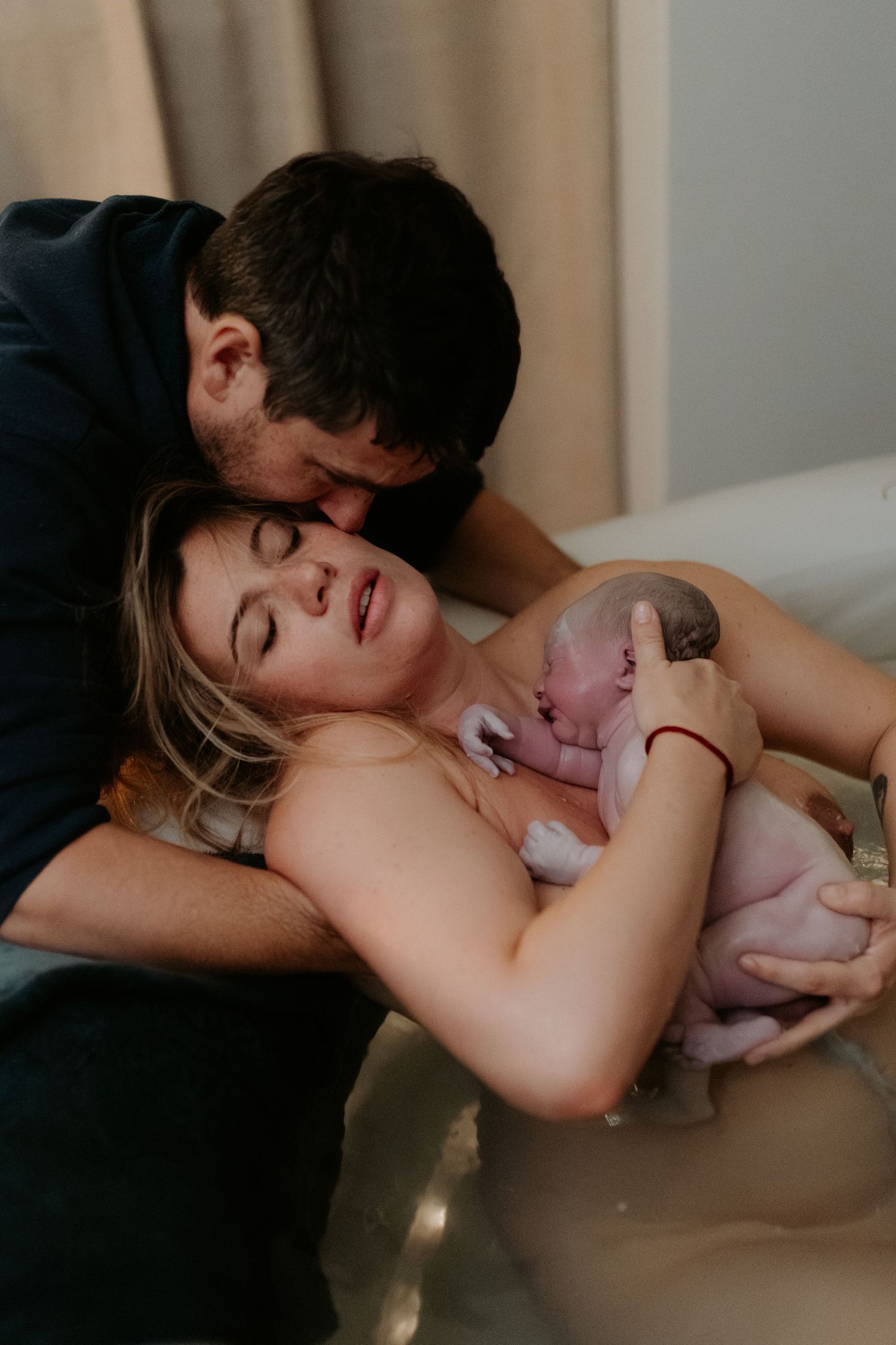 A tender moment during childbirth as a newborn baby is held after delivery while others assist in the background.
