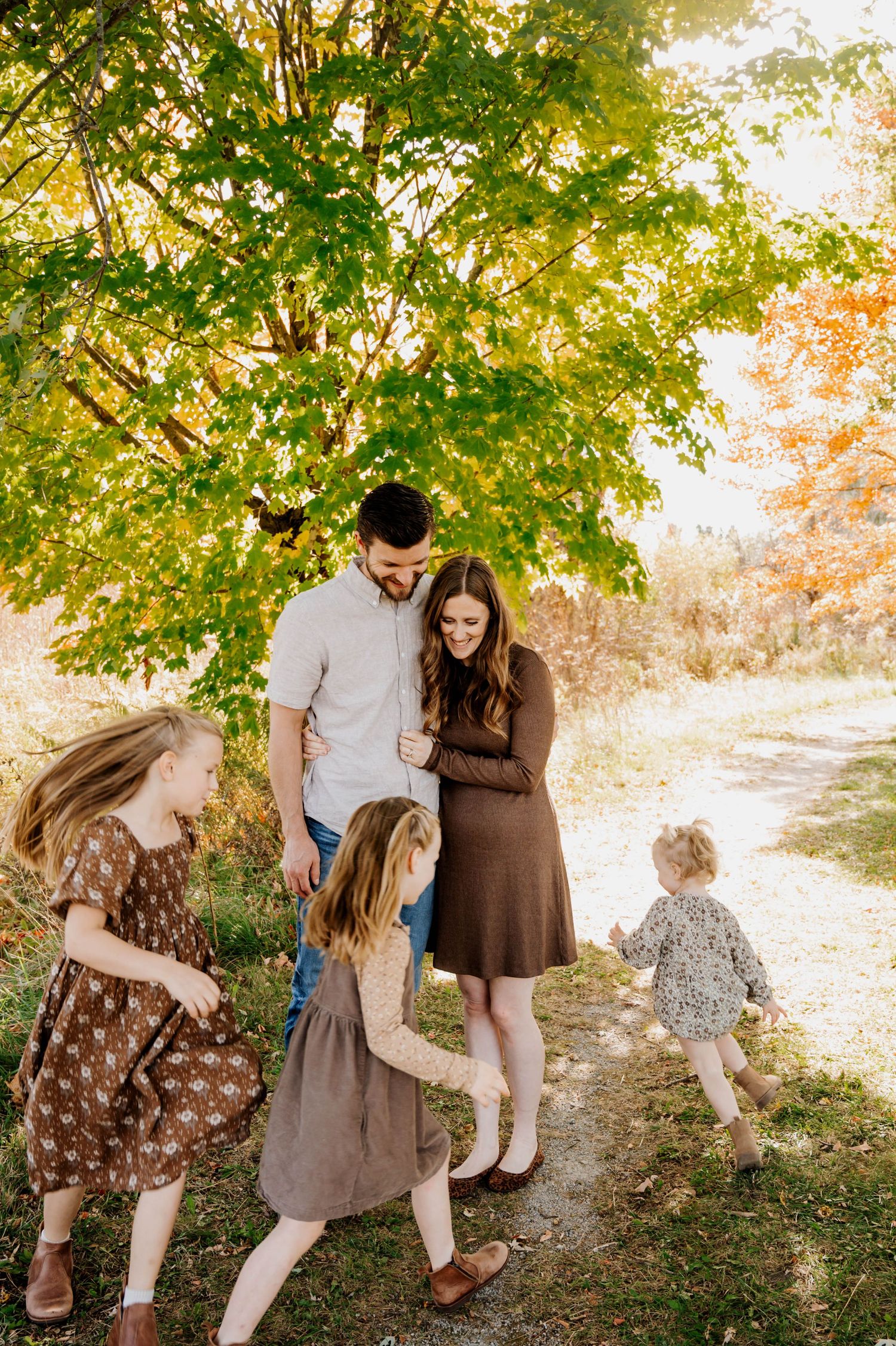 Family walking together on autumn path under golden sunlit trees.