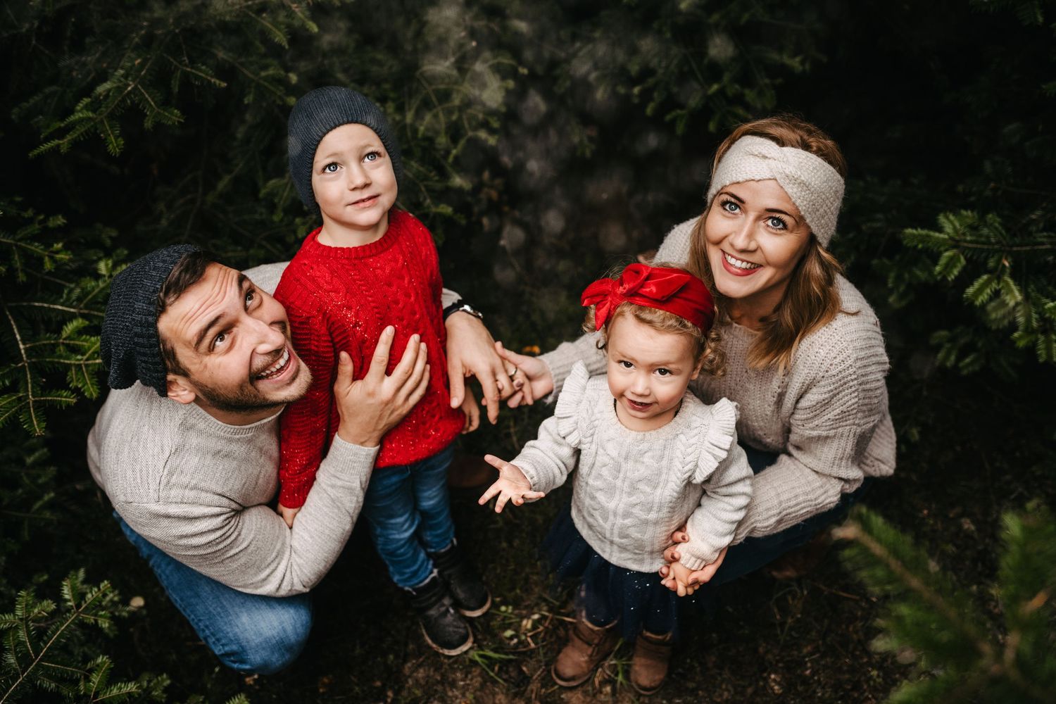 A family enjoying a festive moment among evergreen trees during the holiday season.