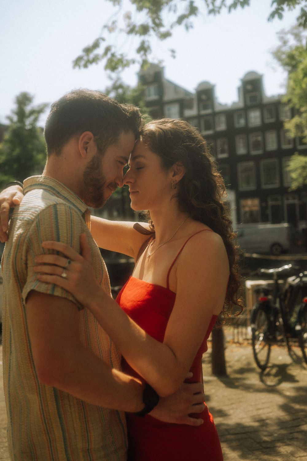 Romantic couple embracing outdoors in warm sunlight near urban buildings.