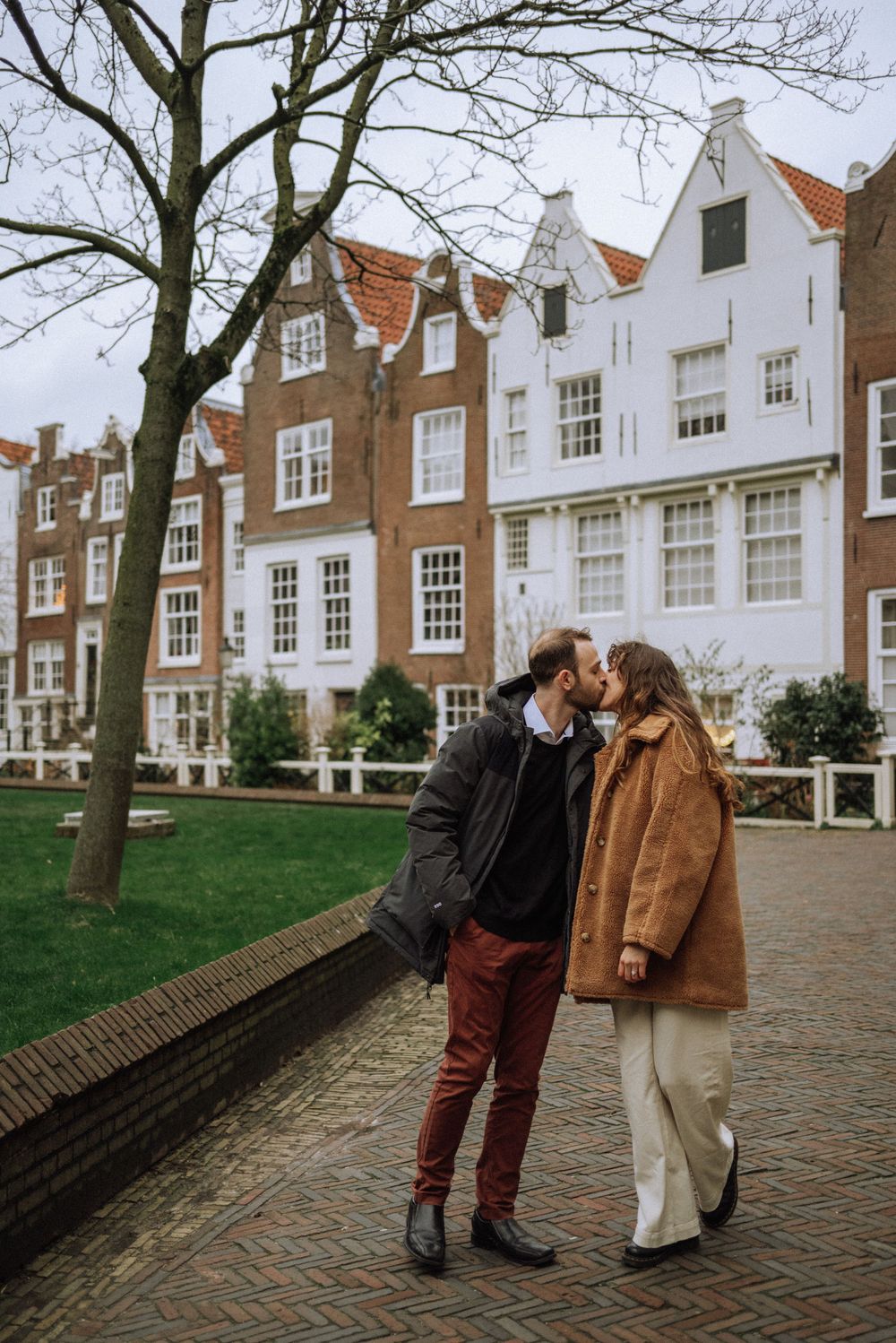 Couple sharing tender moment in front of historic Dutch row houses on cobblestone street.