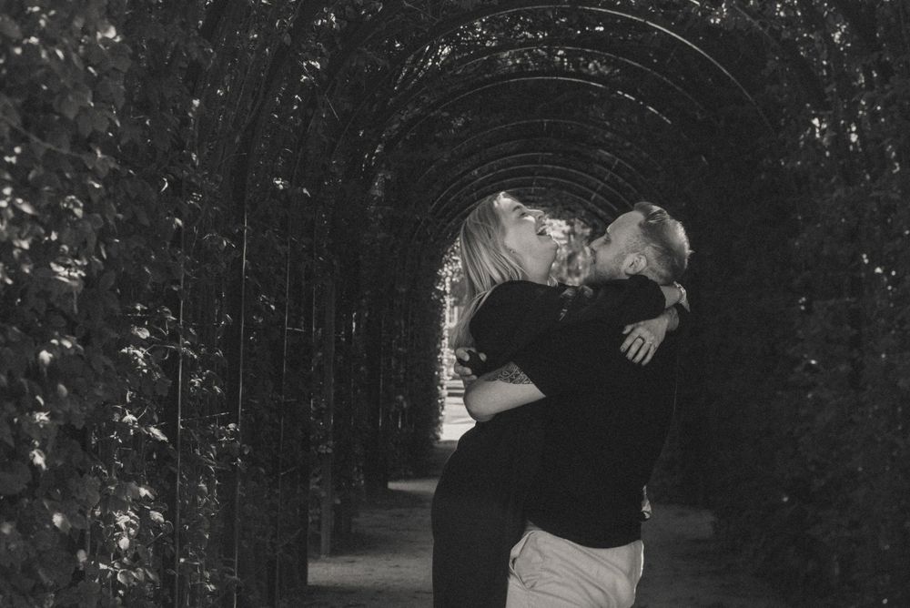 A couple shares intimate black and white moments in a tree-lined pathway.
