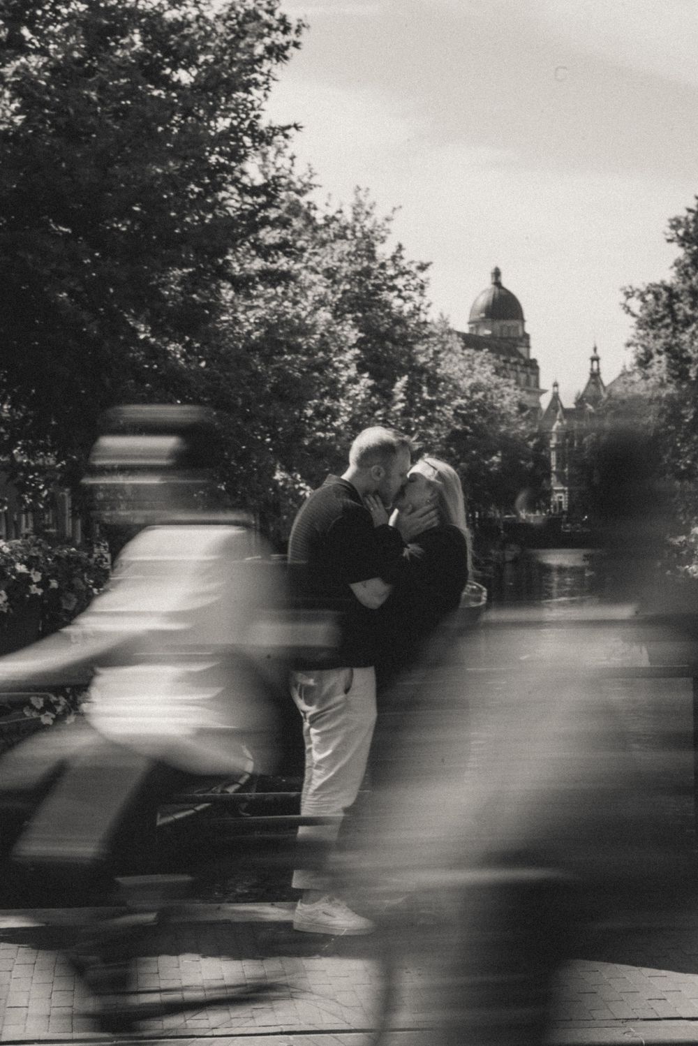 Black and white street scene with motion blur of passing figures against an urban backdrop.