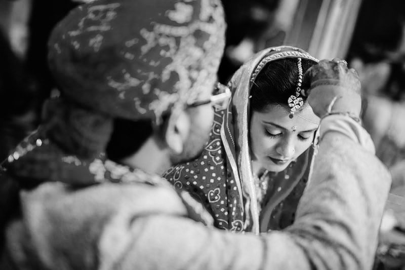 A candid black and white moment during a traditional Indian wedding ceremony showing cultural rituals.