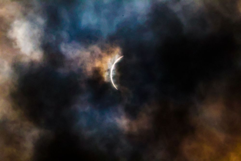 Dramatic view of a solar eclipse with colorful clouds swirling in the dark sky.