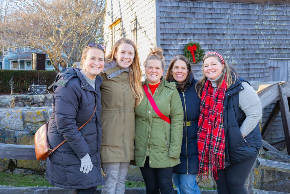 Group of friends in winter coats posing together against rustic building exterior.