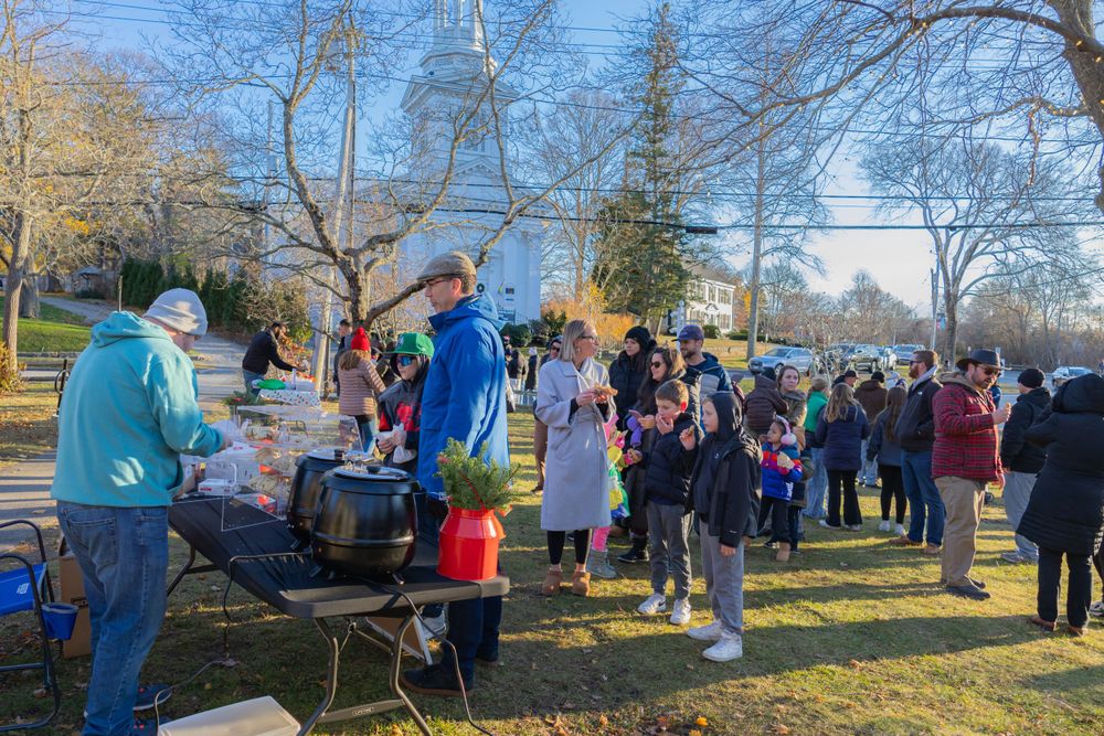 Outdoor community event with food service stations and gathered crowd in winter setting.