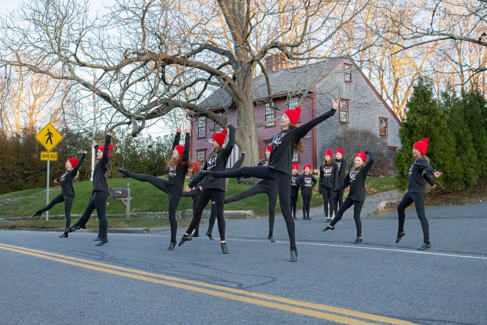 Dance performers in matching outfits perform a synchronized routine on a street.