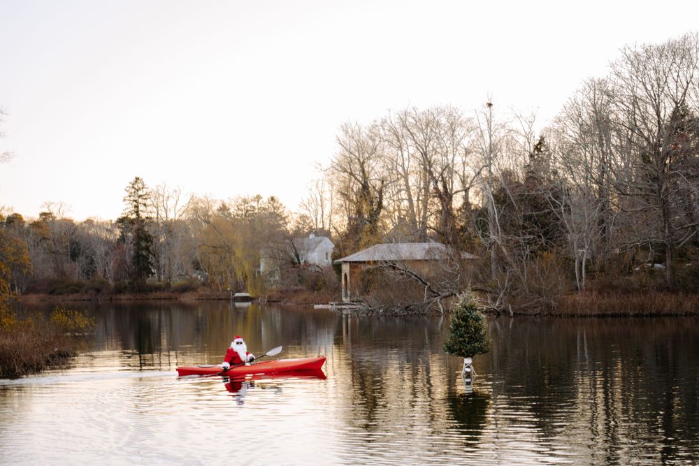 Kayaker paddling on a tranquil winter lake with festive decorations visible along the shoreline.