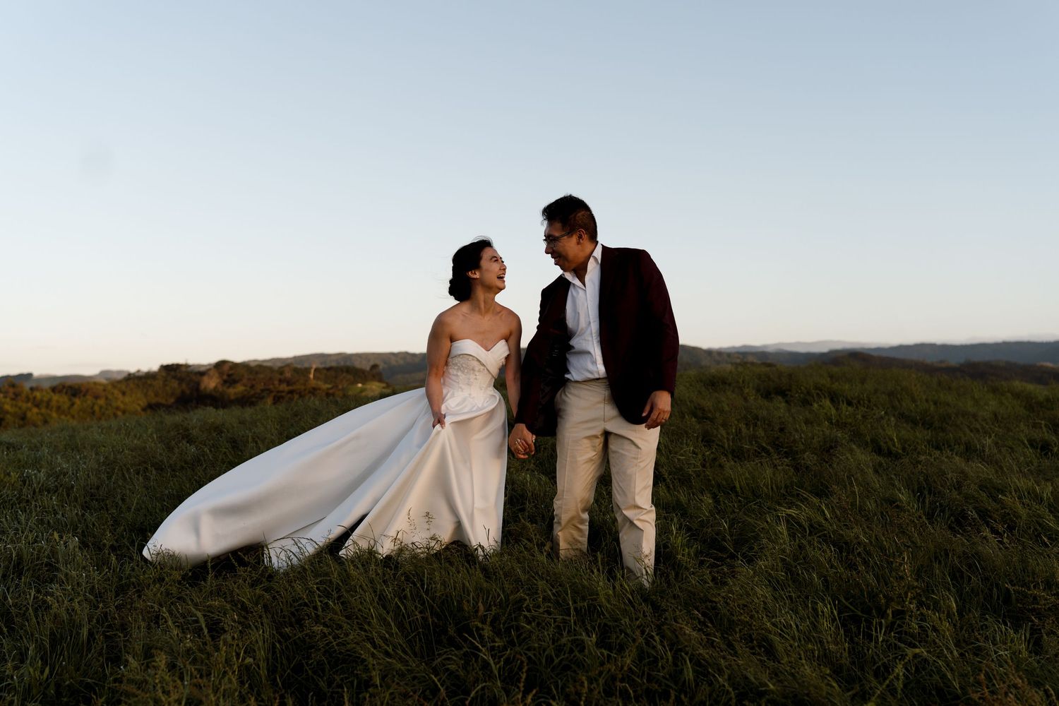 Wedding couple poses in front of stone archway with potted plants and bouquet.