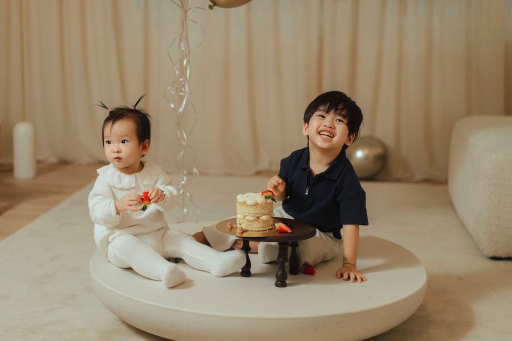 Two young children sit together on a round white platform while a stream of water flows into a clear container.