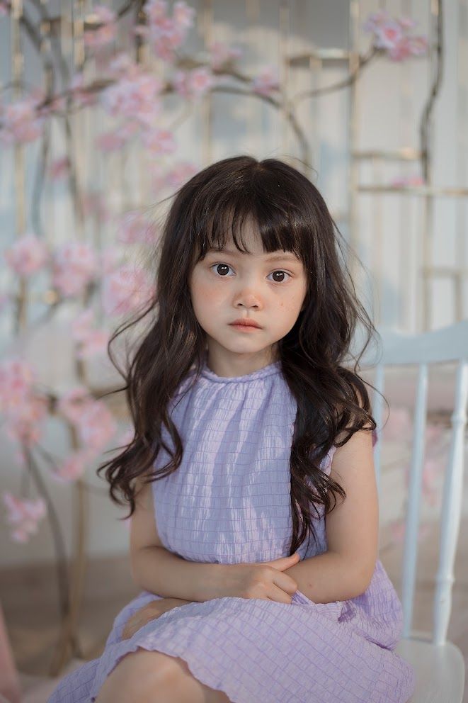 Figure in purple dress poses against backdrop of pink cherry blossoms in soft lighting.