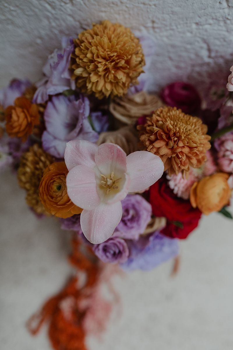 Colorful floral bouquet featuring pink tulips, orange chrysanthemums, purple lisianthus, and red roses with an orange ribbon.