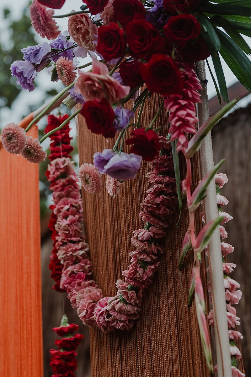 Pink and red floral garland drapes over a textured brown column with purple and crimson blooms above.