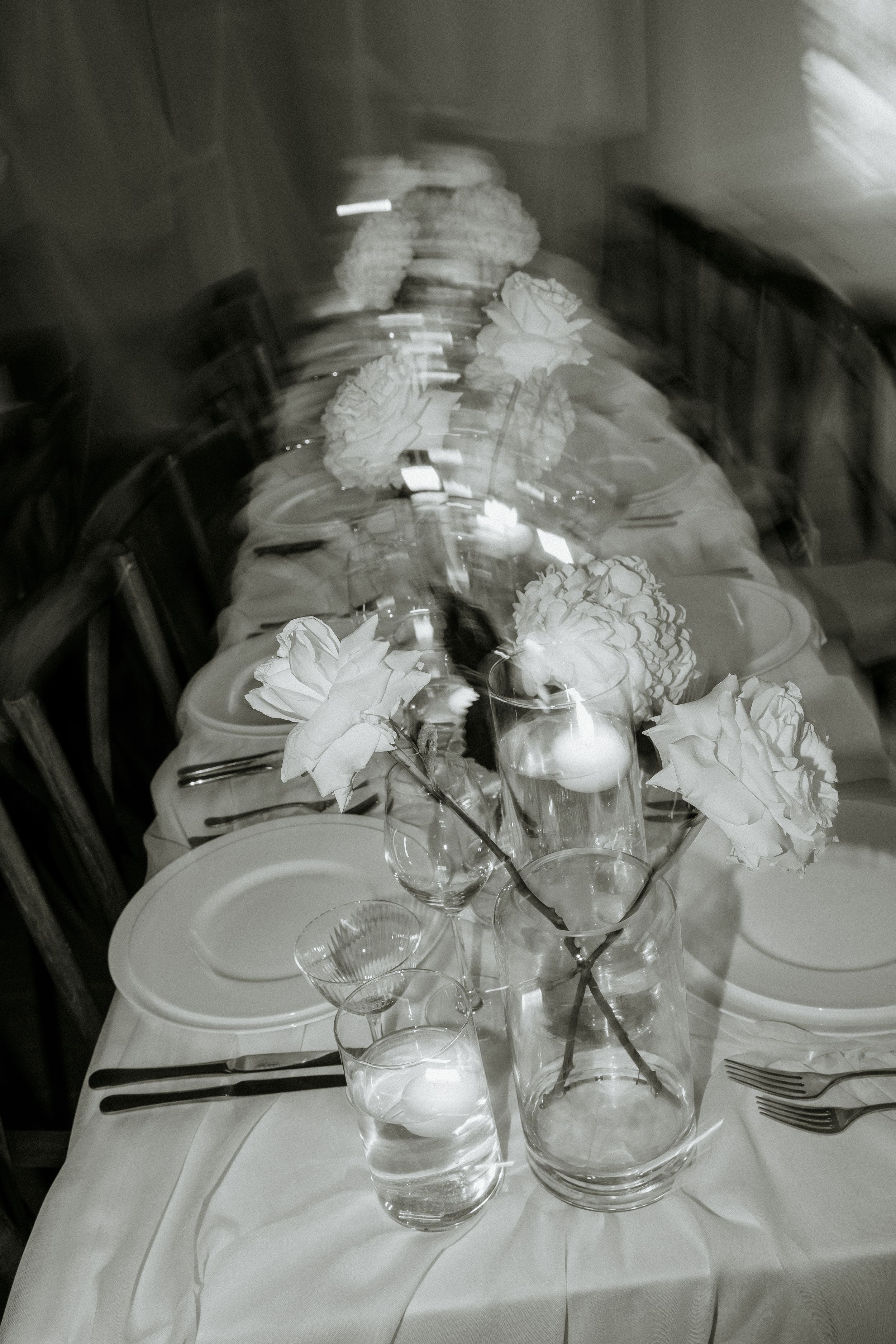 Black and white photo of an elegant table setting with floral centerpieces and place settings.