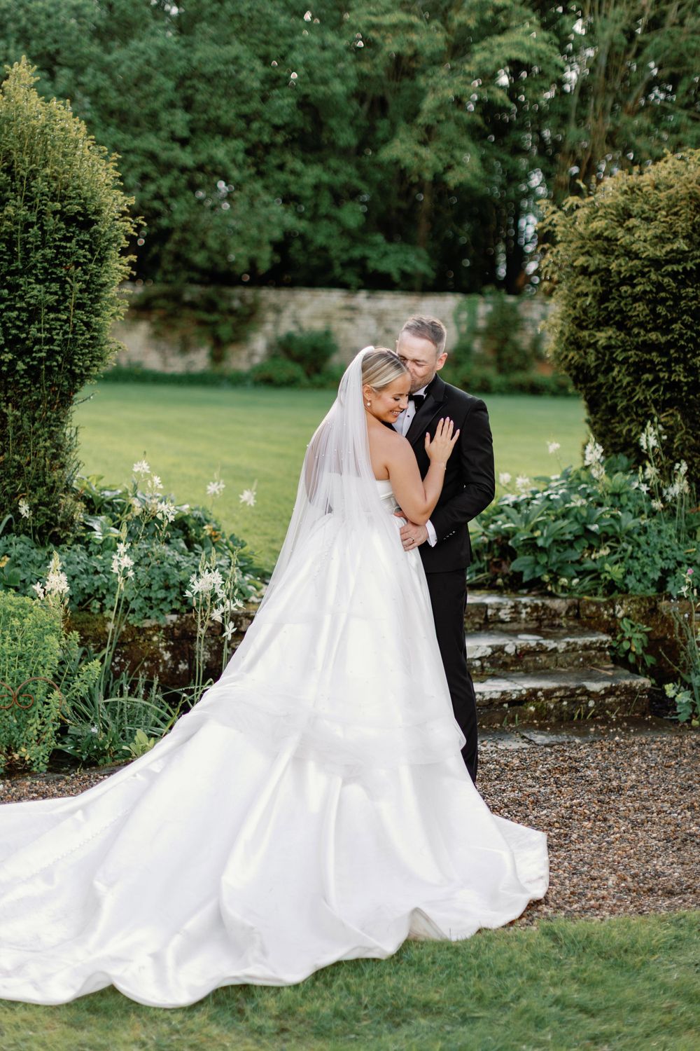 Elegant wedding couple embraces in a lush garden setting with a flowing white bridal gown.