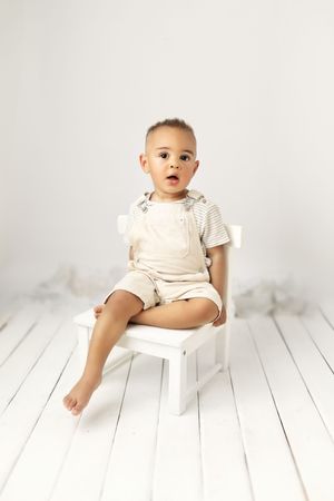 Baby milestone photos showing infant in white outfit sitting on white wooden floor.