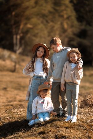 Small children in coordinated outfits sit together on dried grass during golden hour.