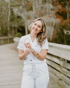 Healthcare professional in white uniform stands on wooden boardwalk amid lush outdoor setting.