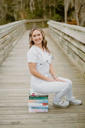 Healthcare professional in white scrubs sitting on medical textbooks on a wooden boardwalk.