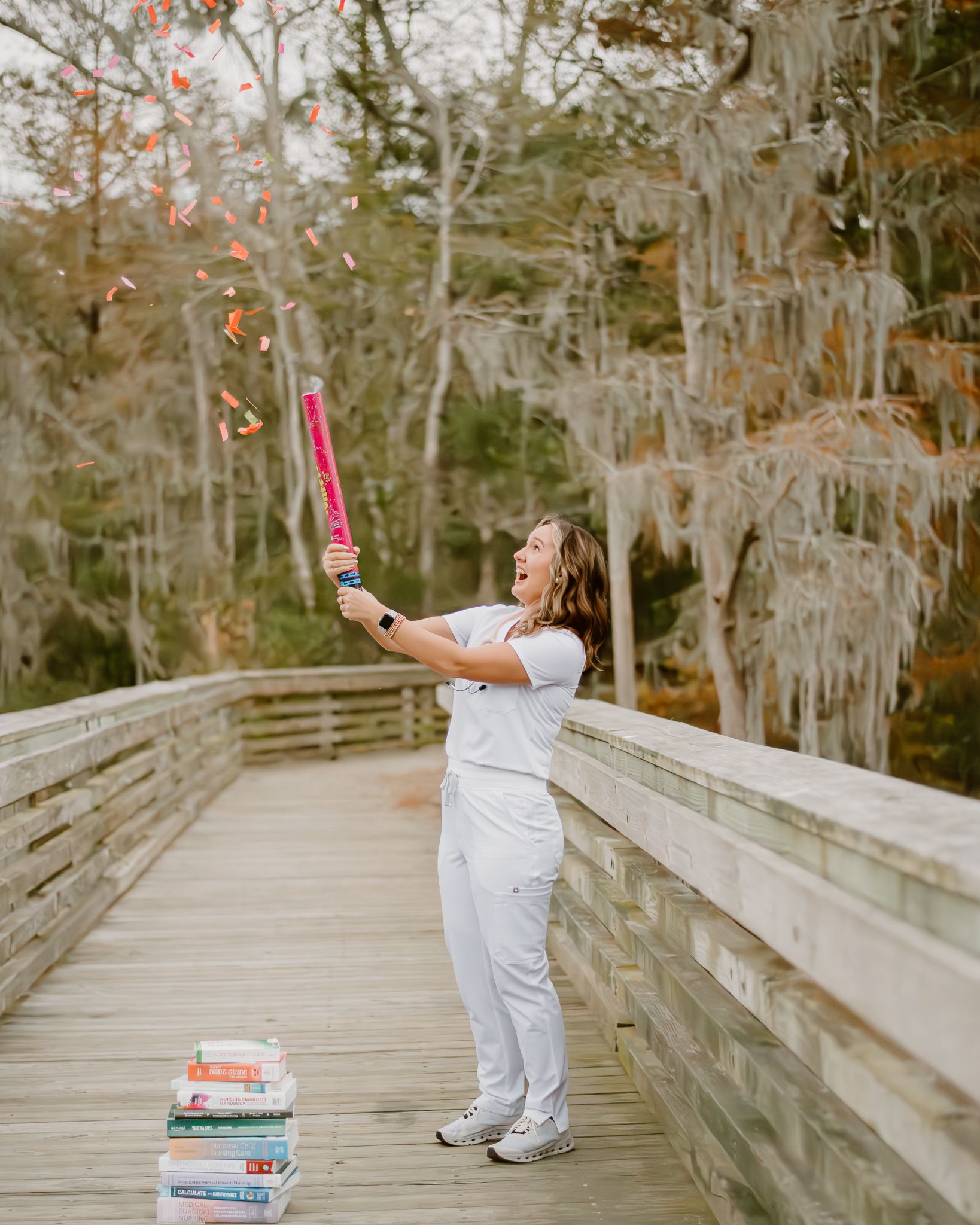 Healthcare professional holding a confetti cannon celebrates on wooden pier with stack of medical books below.
