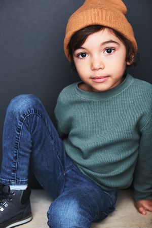 Portrait of a small boy sitting on a box with a beanie.
