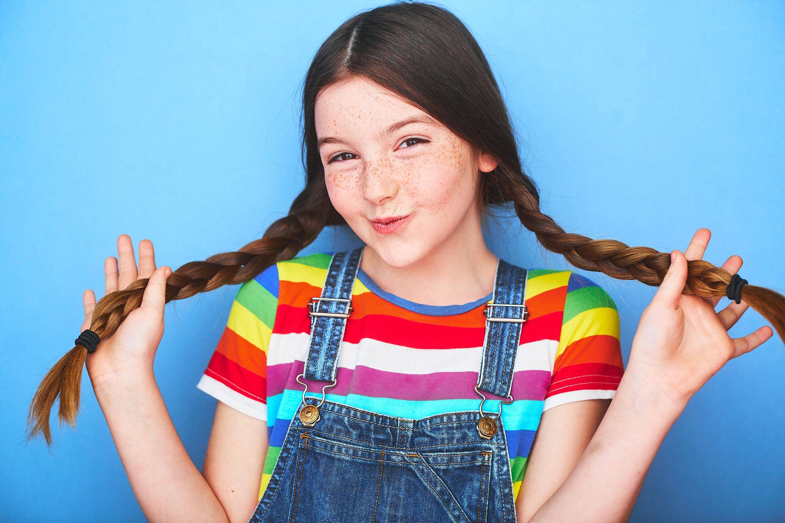 Adorable headshot of a young girl with freckles holding in her hand a braided pigtail on each side of the frame and smiling.
